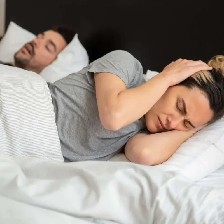 Femme se bouchant les oreilles avec ses mains à cause des bruits nocturnes de son partenaire.